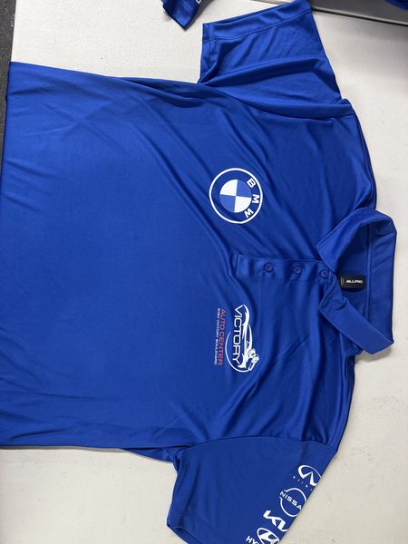 Royal blue performance polo with Victory Auto Center and BMW chest logos and car-brand logos down the sleeve