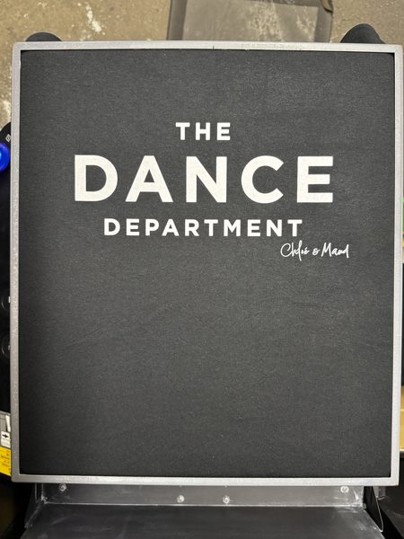 White print reading The Dance Department on a black tee, still on the printer platen