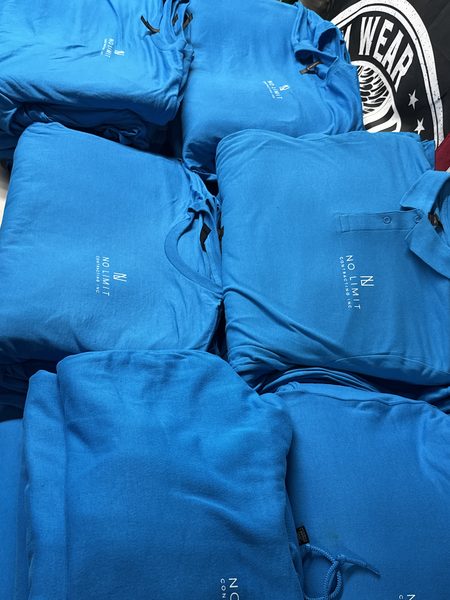 Turquoise tees, polos and hoodies stacked on a table, each with a white No Limit Contracting left-chest logo
