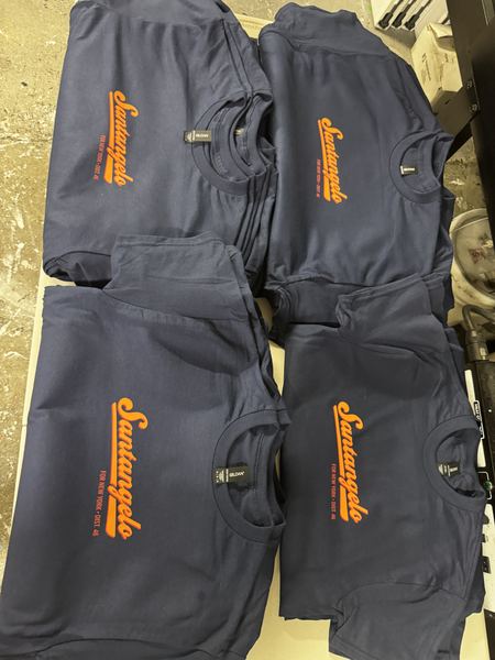 Orange script logo screen printed on navy campaign tees, folded and ready to ship