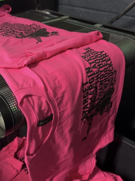 Neon pink tees with a one-color black screen print coming out of a conveyor dryer